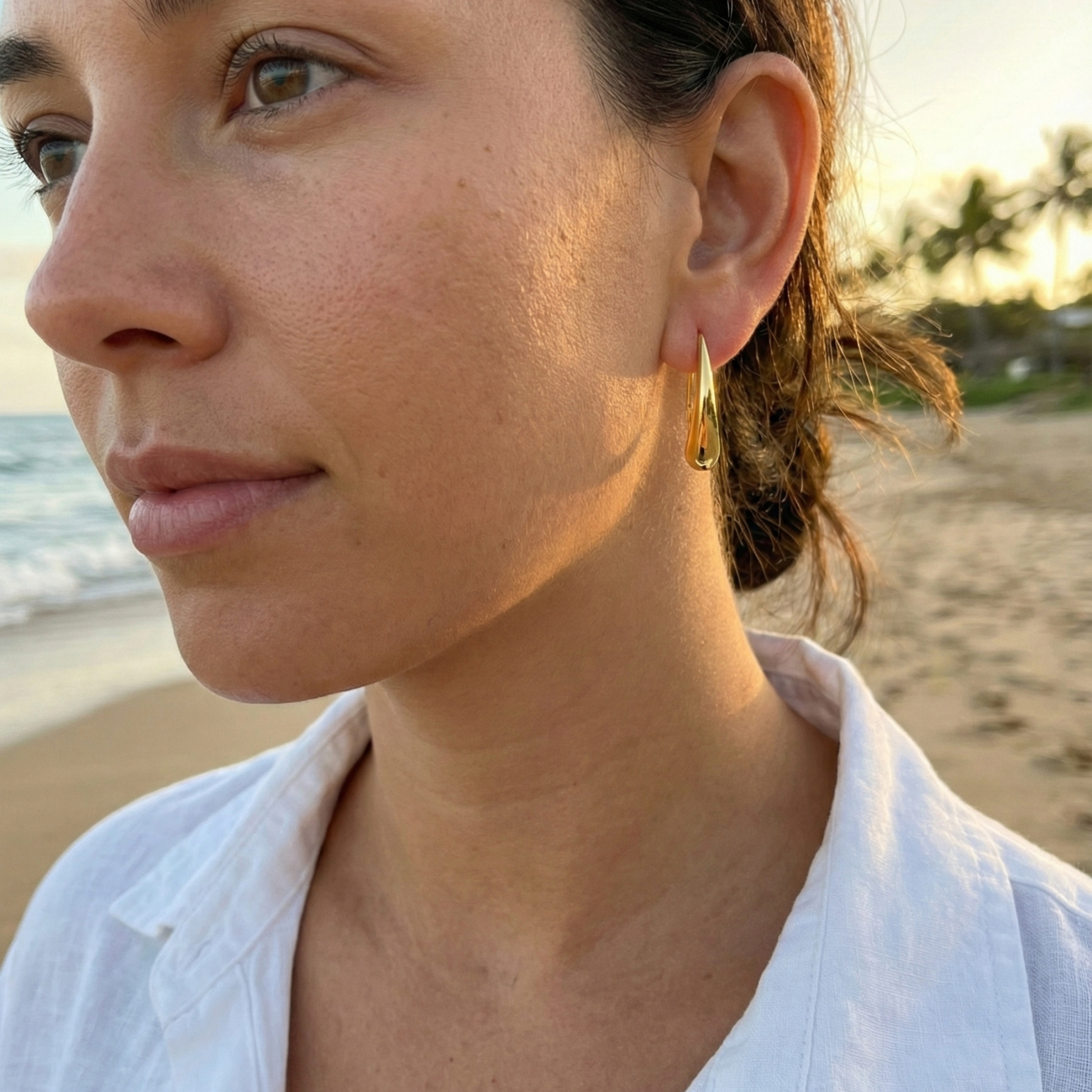 Pair of polished gold tapered raindrop earrings with elongated hook design on white background.