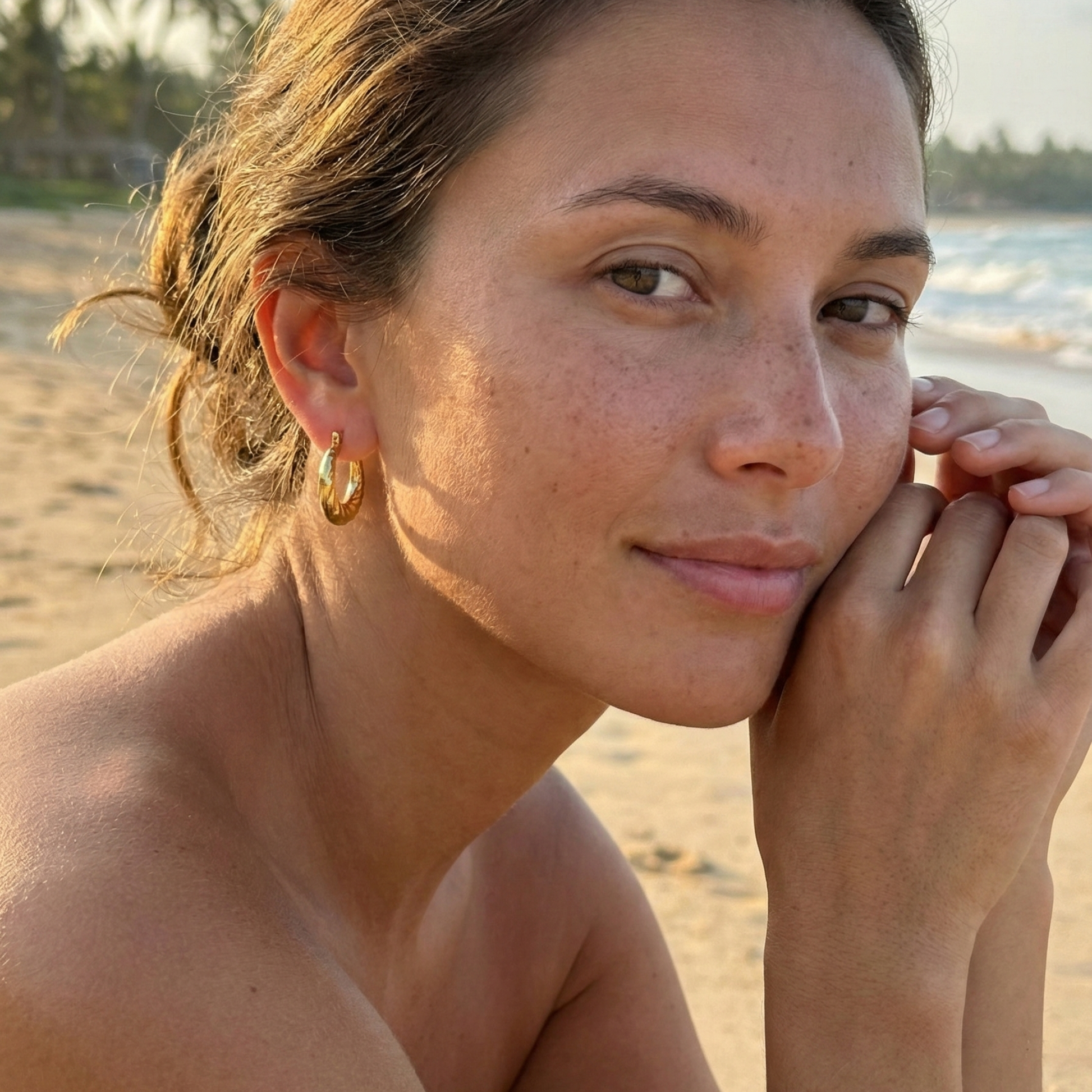 Molten Swirl Gold Hoop Earrings on a model, beach background