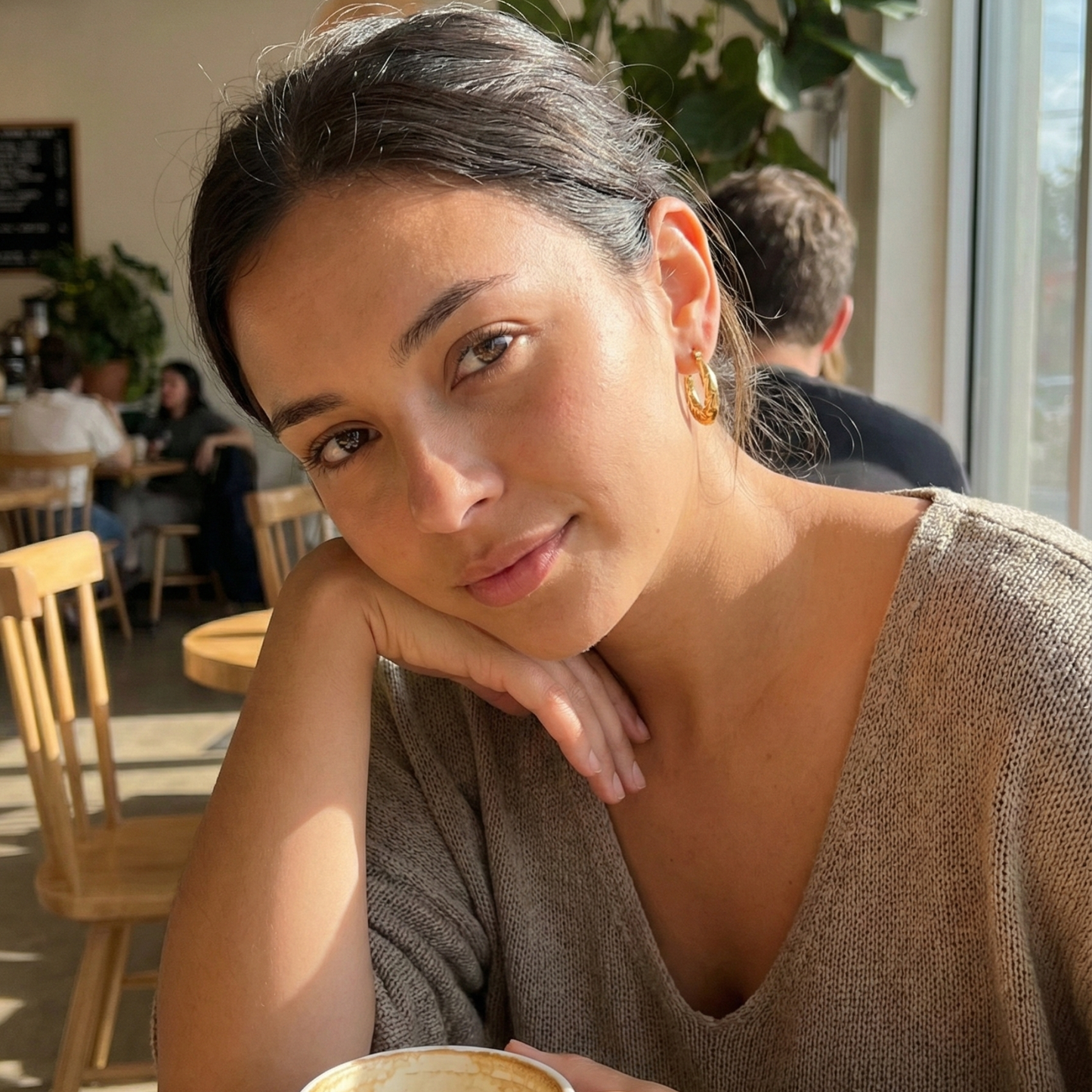 Molten Swirl Gold Hoop Earrings on a model, cafe background