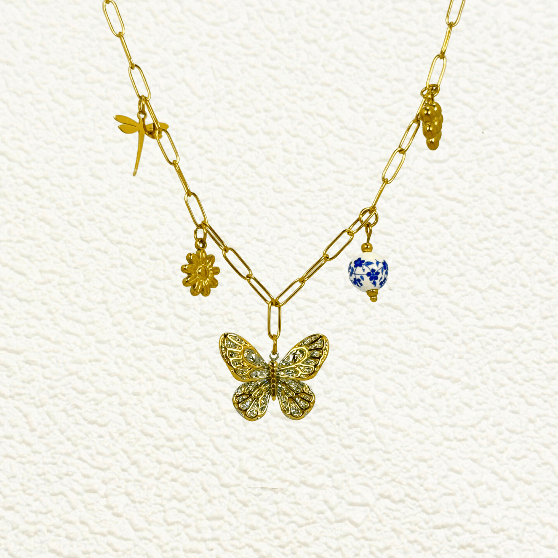 Gold charm necklace with butterfly, daisy, dragonfly, grape, and blue floral bead on waterproof paperclip chain