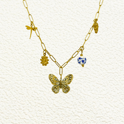 Gold charm necklace with butterfly, daisy, dragonfly, grape, and blue floral bead on waterproof paperclip chain