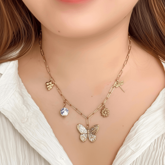 Gold charm necklace with butterfly, daisy, dragonfly, grape, and blue floral bead on waterproof paperclip chain