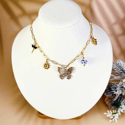 Gold charm necklace with butterfly, daisy, dragonfly, grape, and blue floral bead on waterproof paperclip chain