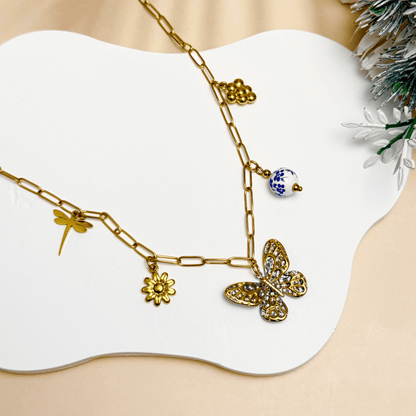 Gold charm necklace with butterfly, daisy, dragonfly, grape, and blue floral bead on waterproof paperclip chain