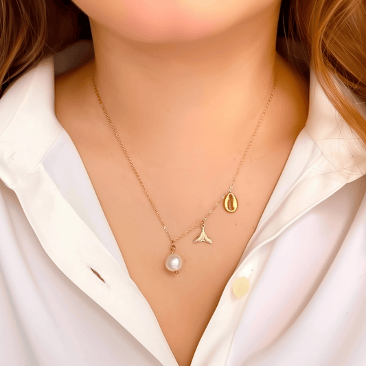 Gold necklace with pearl, whale tail, and shell charms on dainty waterproof chain