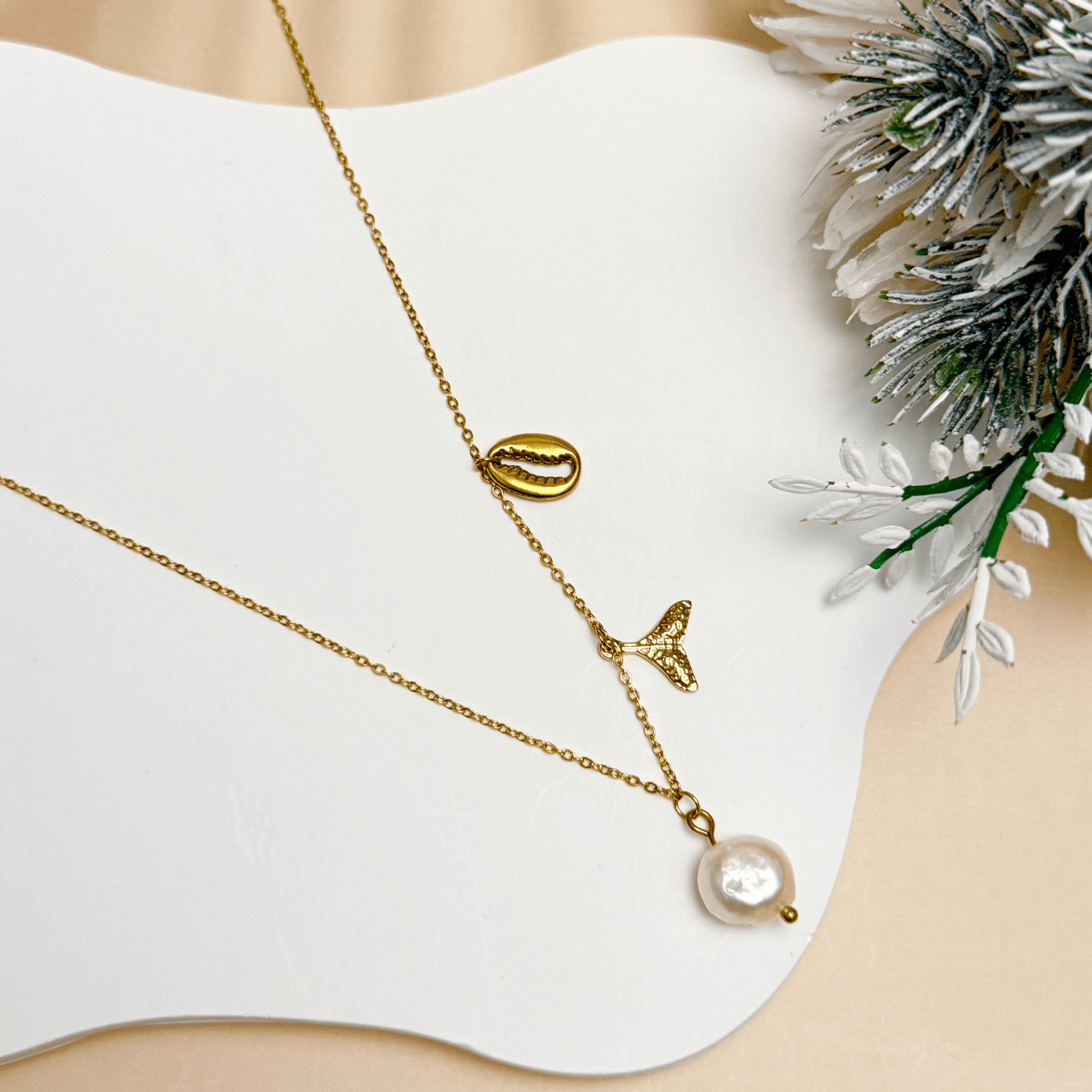 Gold necklace with pearl, whale tail, and shell charms on dainty waterproof chain