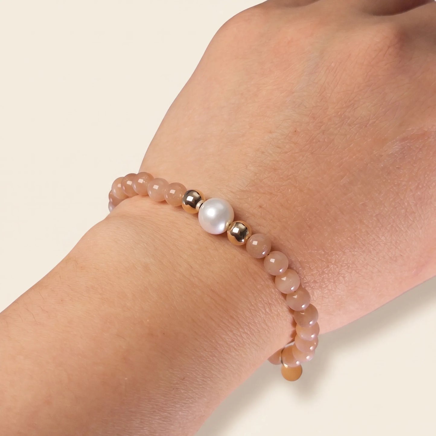 A beaded bracelet featuring peach moonstone beads, premium freshwater pearl, and a stamped initial disc, 14k gold filled. MXW Jewellery