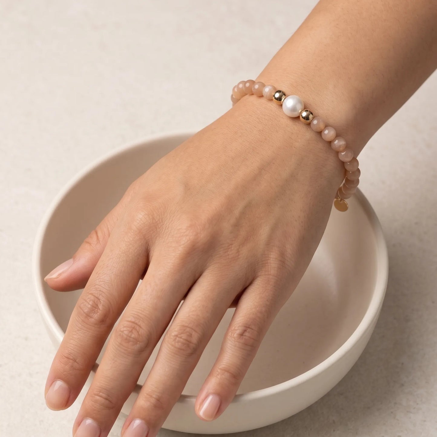 A beaded bracelet featuring peach moonstone beads, premium freshwater pearl, and a stamped initial disc, 14k gold filled. MXW Jewellery