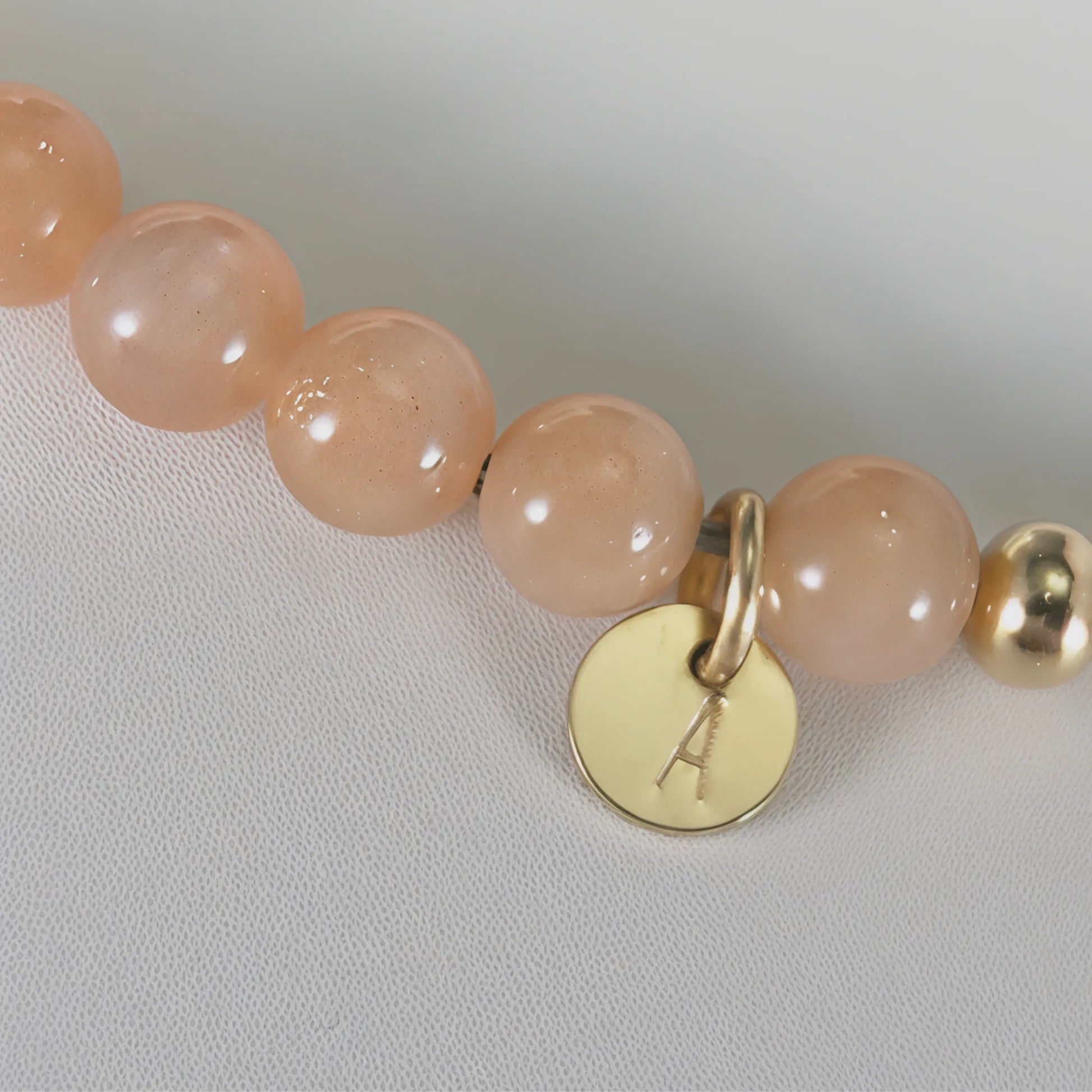 A beaded bracelet featuring peach moonstone beads, premium freshwater pearl, and a stamped initial disc, 14k gold filled. MXW Jewellery