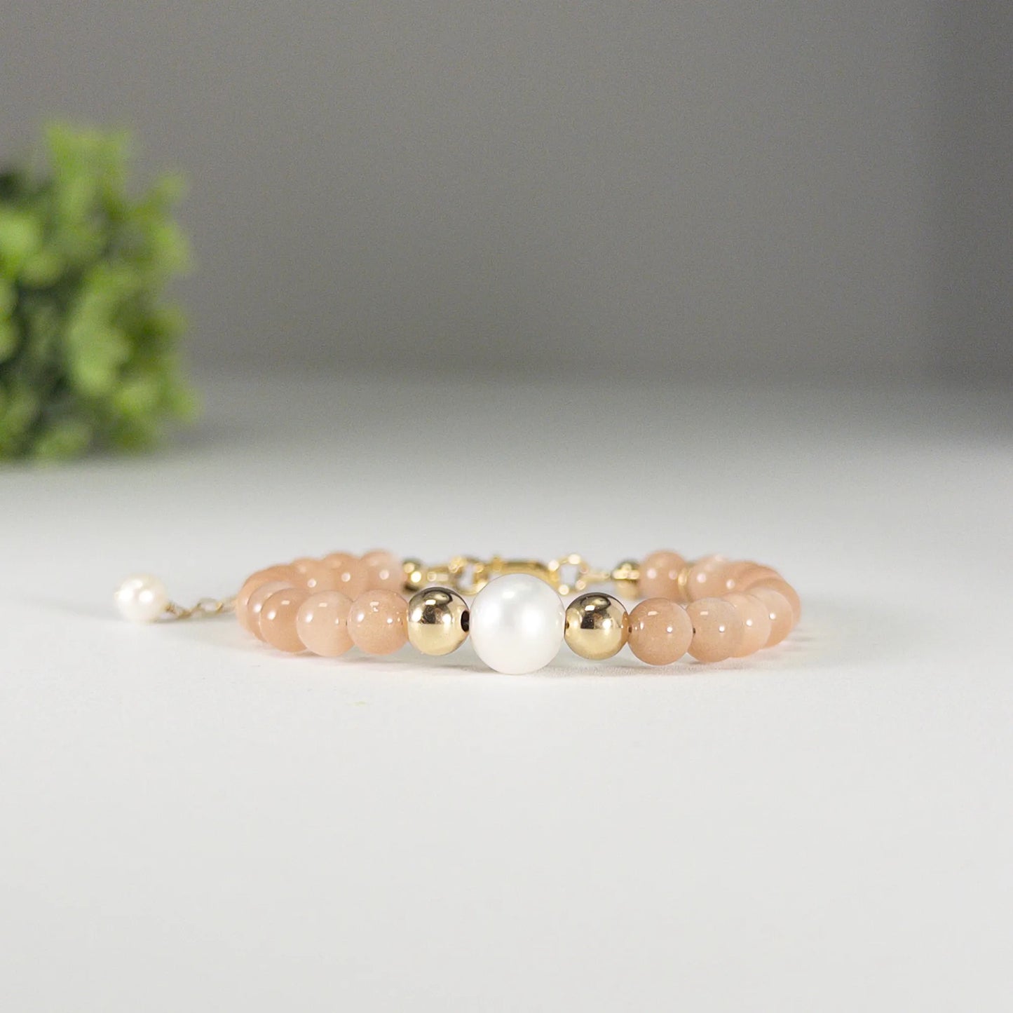A beaded bracelet featuring peach moonstone beads, premium freshwater pearl, and a stamped initial disc, 14k gold filled. MXW Jewellery