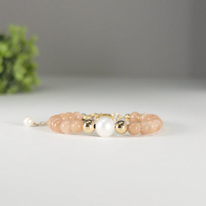 A beaded bracelet featuring peach moonstone beads, premium freshwater pearl, and a stamped initial disc, 14k gold filled. MXW Jewellery