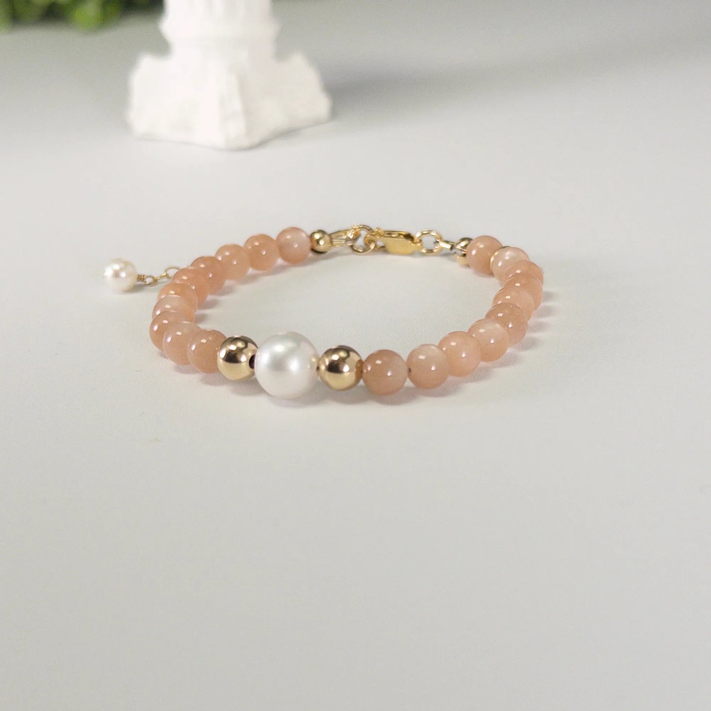A beaded bracelet featuring peach moonstone beads, premium freshwater pearl, and a stamped initial disc, 14k gold filled. MXW Jewellery