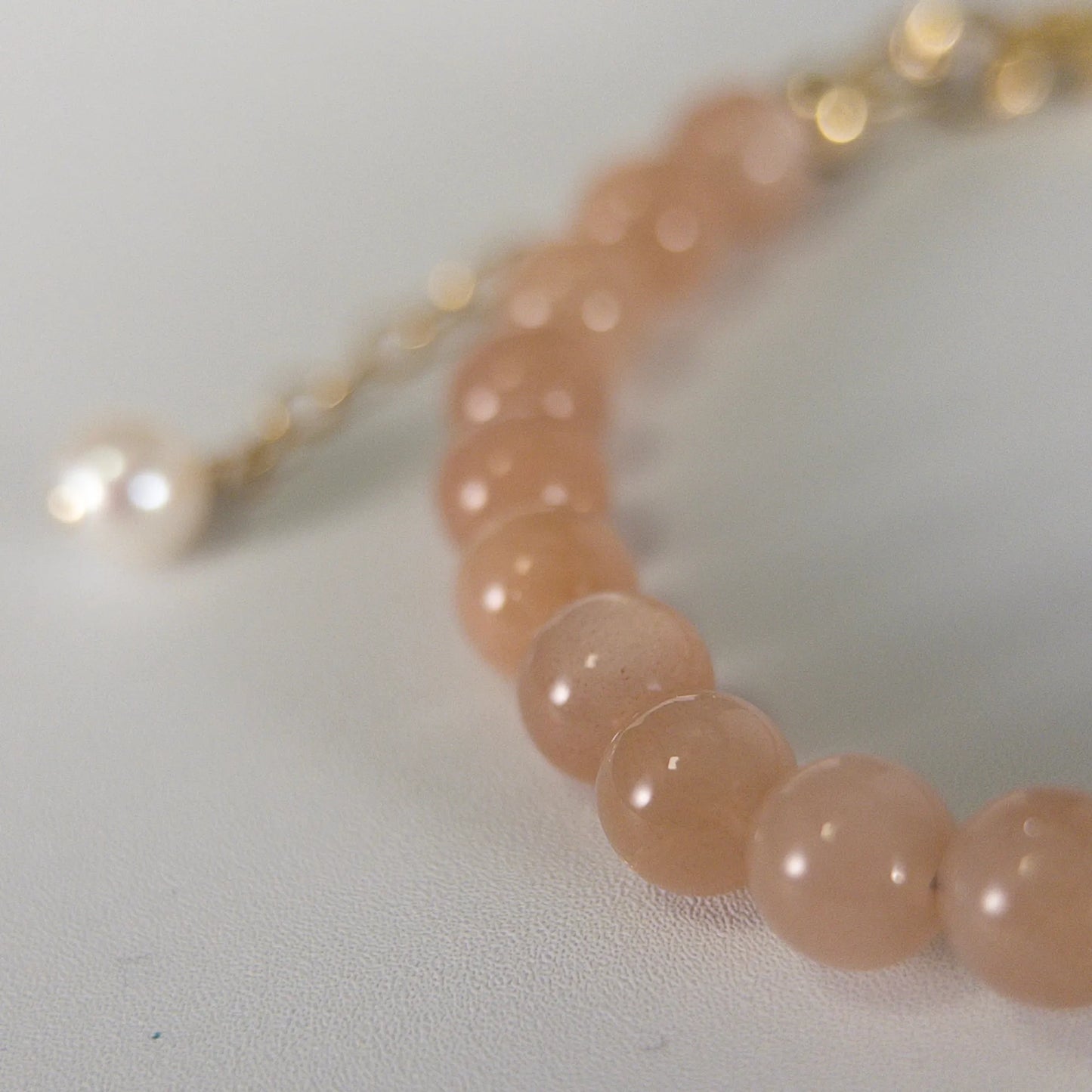 A beaded bracelet featuring peach moonstone beads, premium freshwater pearl, and a stamped initial disc, 14k gold filled. MXW Jewellery