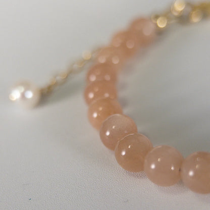 A beaded bracelet featuring peach moonstone beads, premium freshwater pearl, and a stamped initial disc, 14k gold filled. MXW Jewellery