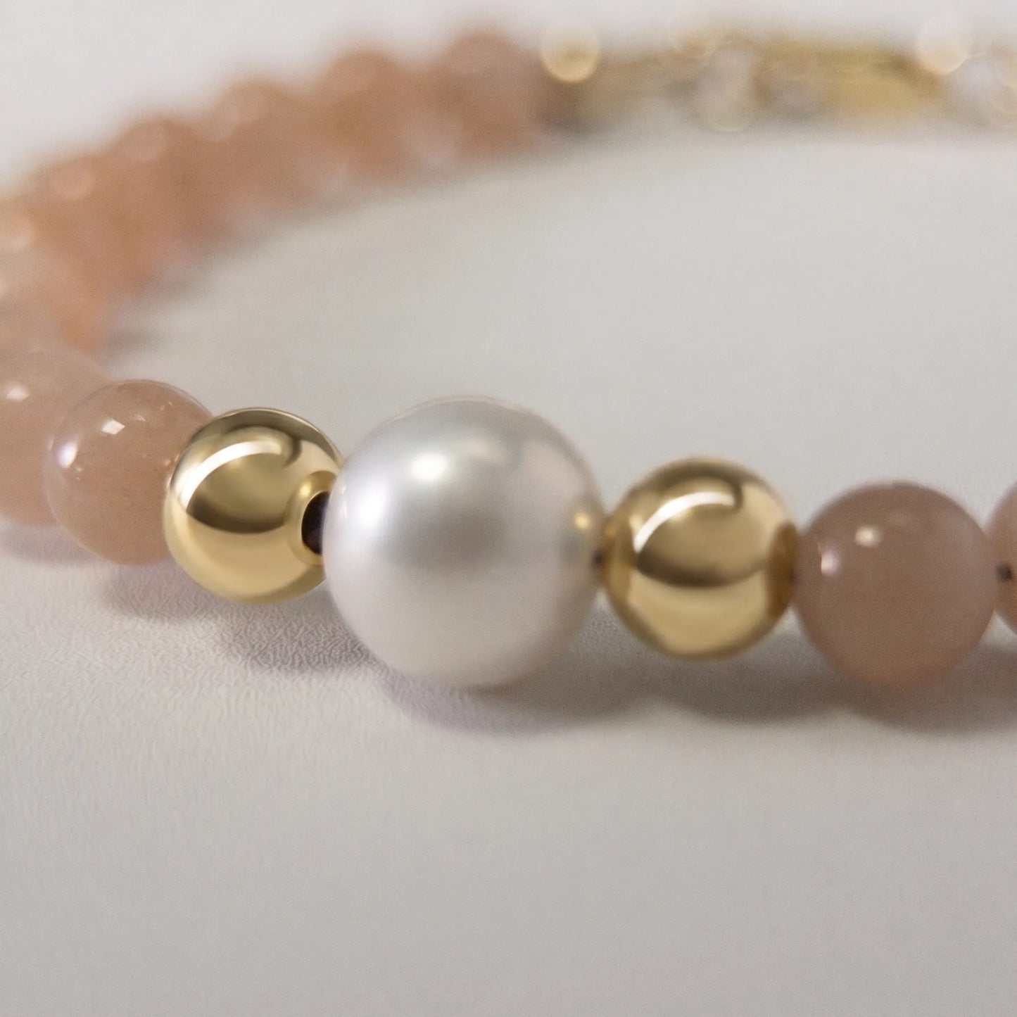 A beaded bracelet featuring peach moonstone beads, premium freshwater pearl, and a stamped initial disc, 14k gold filled. MXW Jewellery