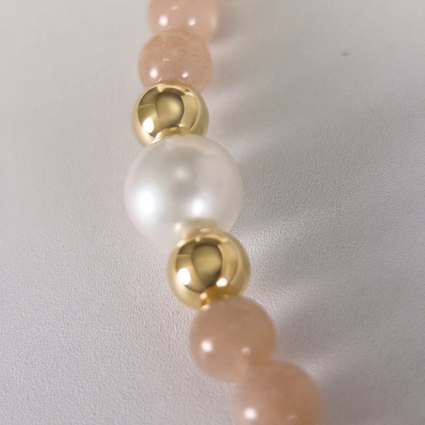 A beaded bracelet featuring peach moonstone beads, premium freshwater pearl, and a stamped initial disc, 14k gold filled. MXW Jewellery