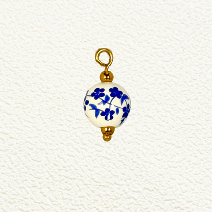 Round white ceramic charm with delicate blue flower and vine pattern, finished with gold accents