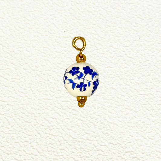 Round white ceramic charm with delicate blue flower and vine pattern, finished with gold accents