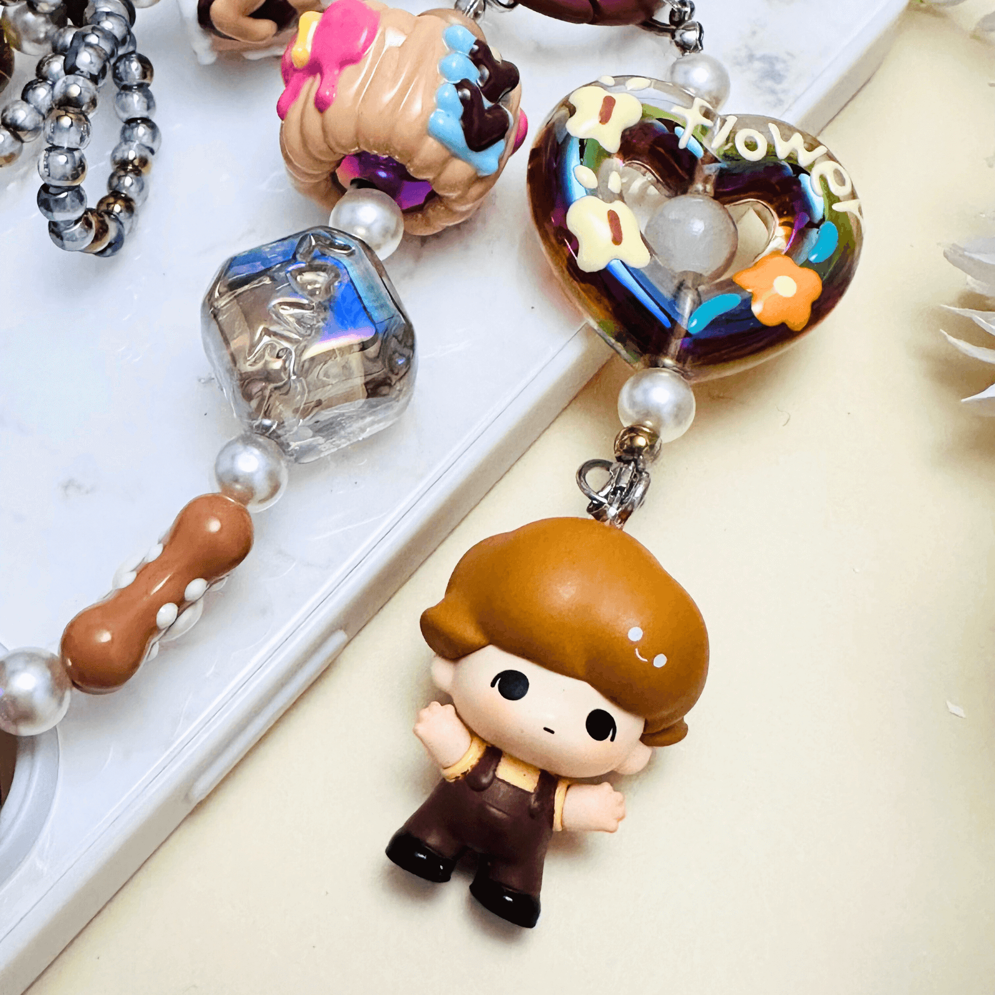 Handmade Pop Bean Brown Dimoo phone charm with hand-painted polymer clay beads and faux pearls, attached to a keychain.