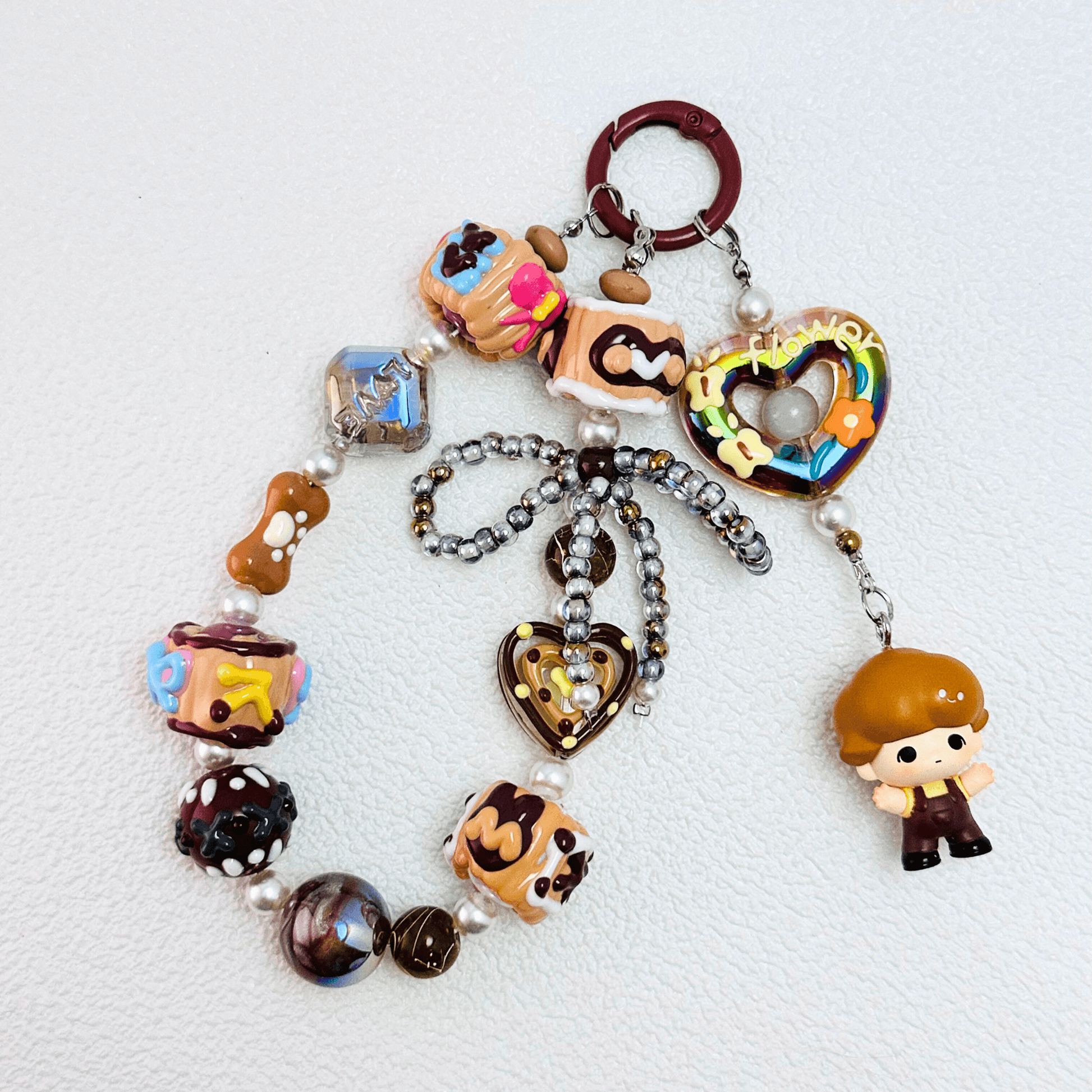 Handmade Pop Bean Brown Dimoo phone charm with hand-painted polymer clay beads and faux pearls, attached to a keychain.
