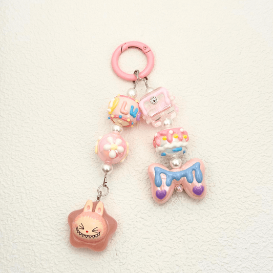 Pop Bean Labubu handmade phone charm in pink star theme, featuring kawaii beads, flowers, and a playful character, attached to a white marble phone case – cute accessory by MXW Jewellery