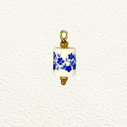 Cylindrical white ceramic charm with blue floral design and gold detailing