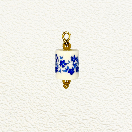 Cylindrical white ceramic charm with blue floral design and gold detailing