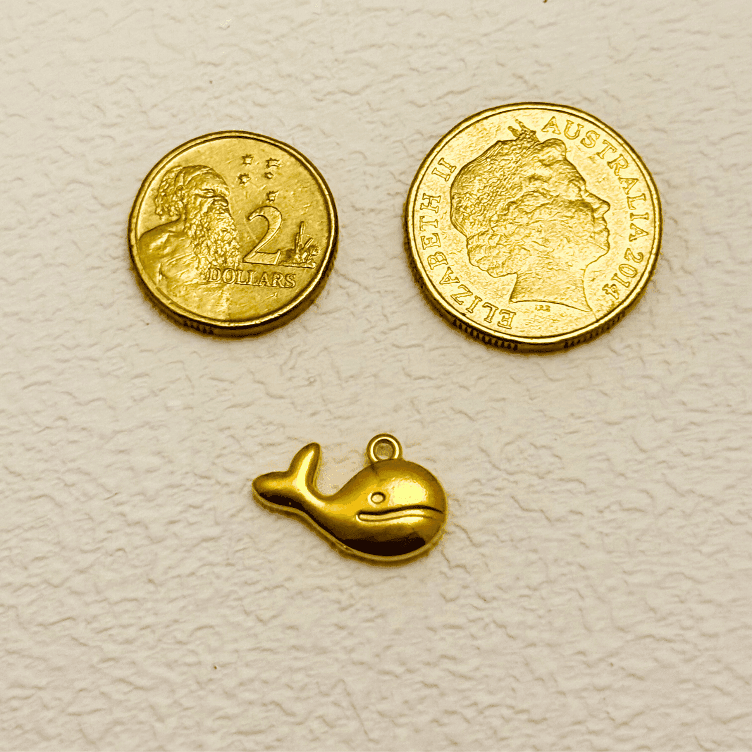 Gold whale charm with a smiling face and curved tail, PVD gold plated finish