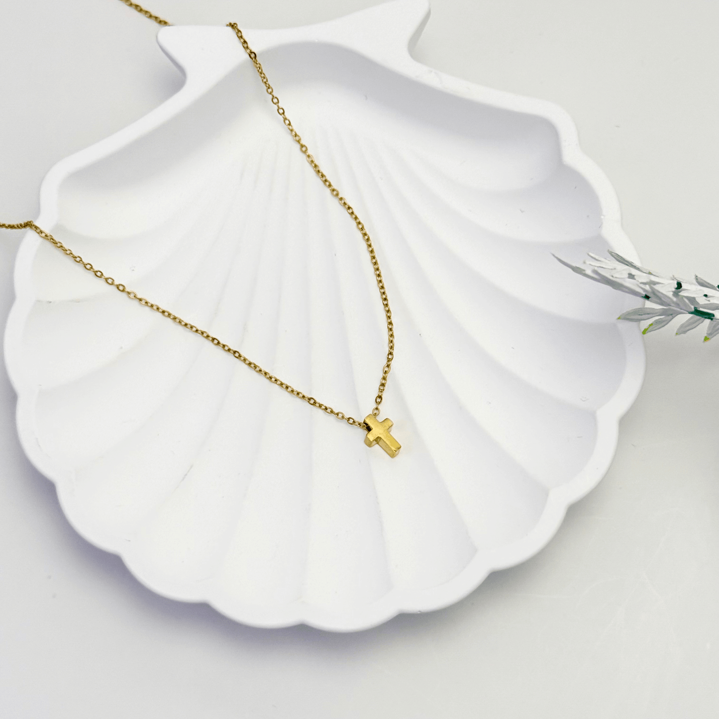 Gold necklace with a small cross pendant on a white shell