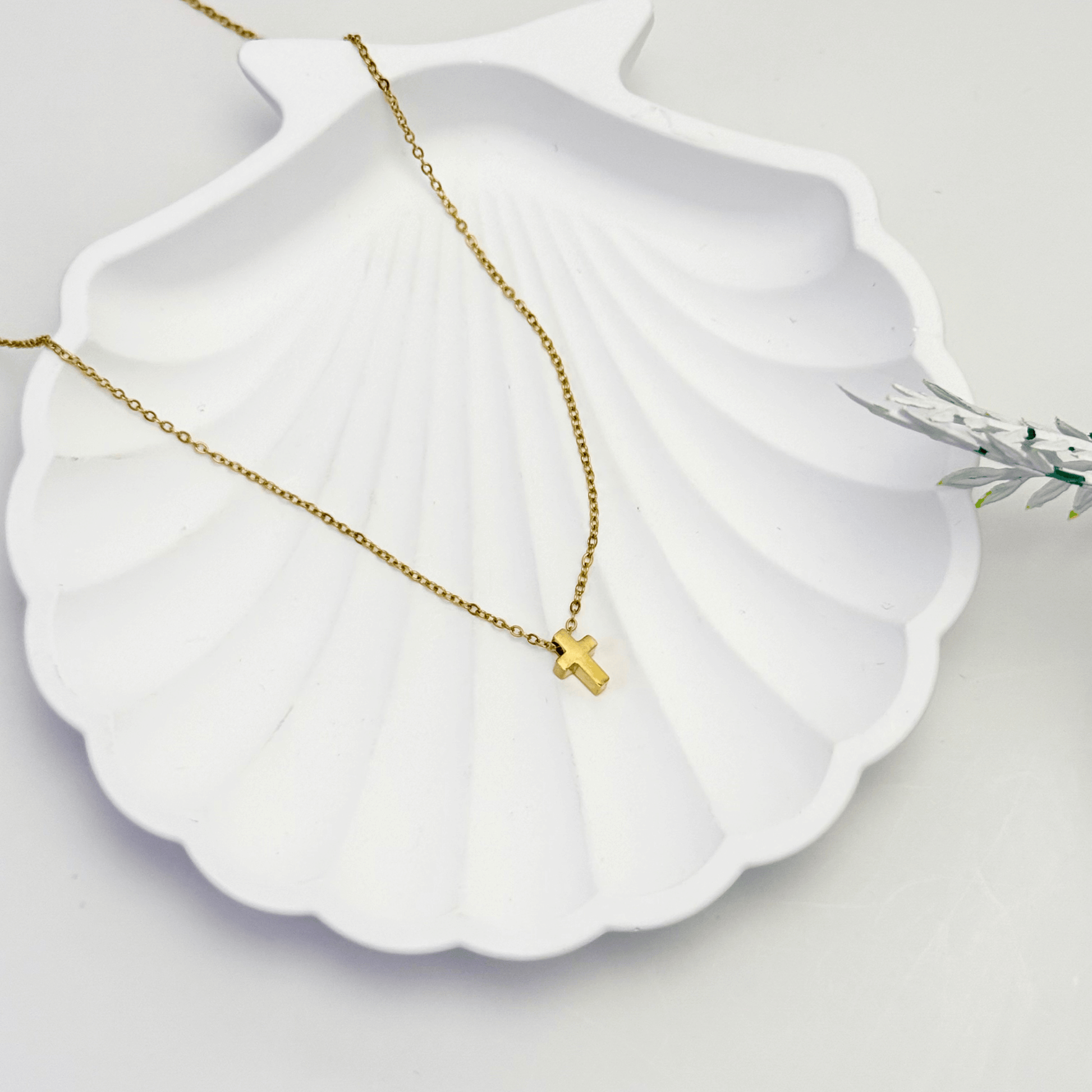 Gold necklace with a small cross pendant on a white shell