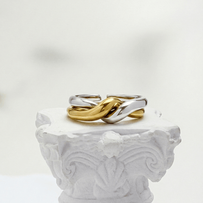Two-Tone Interlocking Ring by MXW Jewellery featuring interwoven gold and silver bands displayed on a white textured pedestal.
