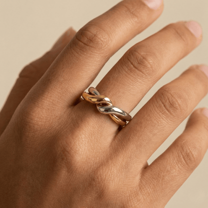 Two-Tone Interlocking Ring by MXW Jewellery featuring interwoven gold and silver bands displayed on a white textured pedestal.