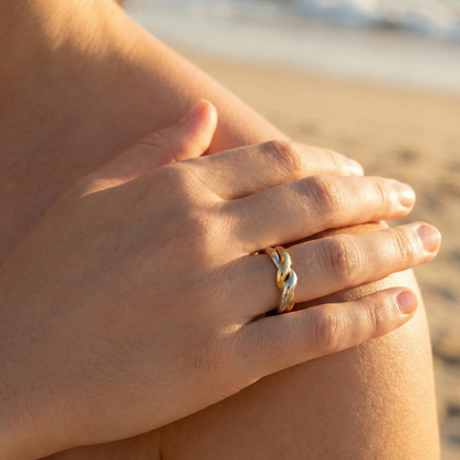 Two-Tone Interlocking Ring by MXW Jewellery featuring interwoven gold and silver bands displayed on a white textured pedestal.